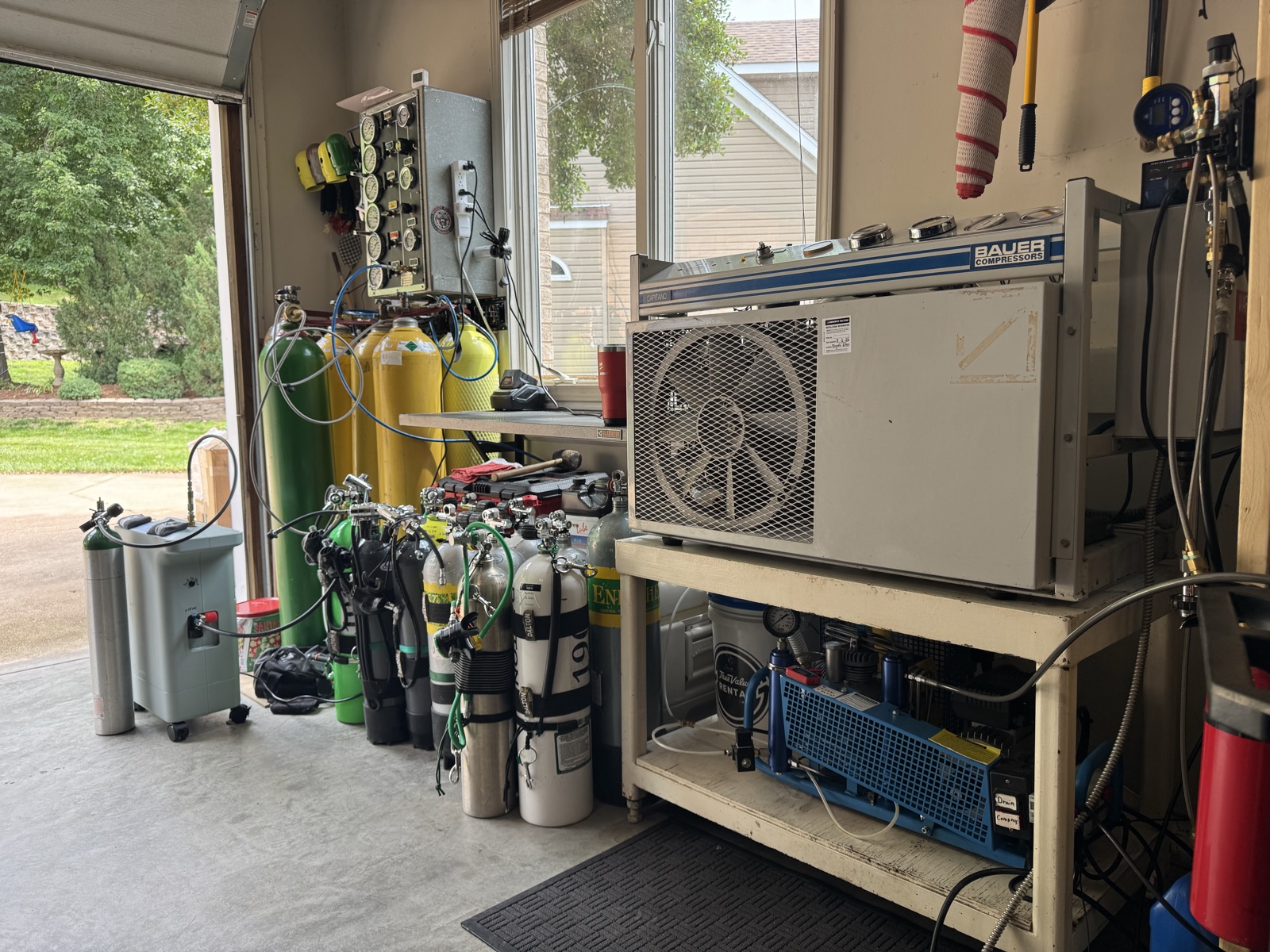 SoCo Tech Diving's fill bench: a Bauer breathing-air compressor beside a rack of steel and aluminum dive cylinders and assembled regulators, with daylight coming through the bay window.